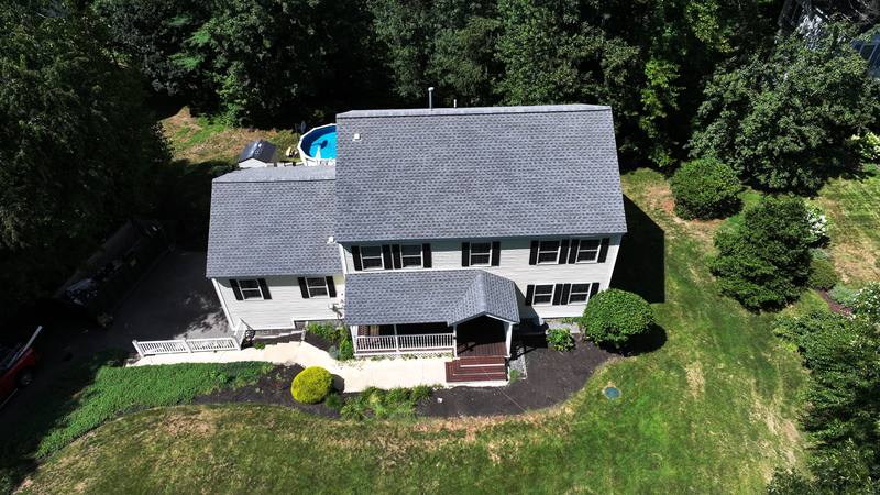 White colonial with a gray shingle roof and front porch, aerial view