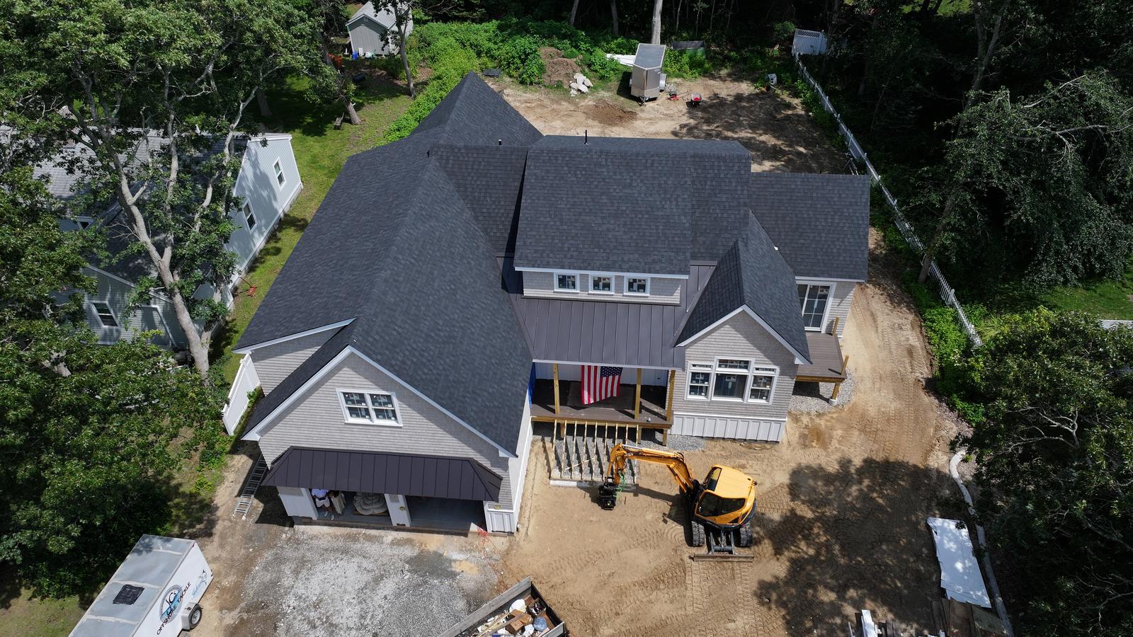 New construction home with a dark shingle roof and gray siding, deck stairs underway