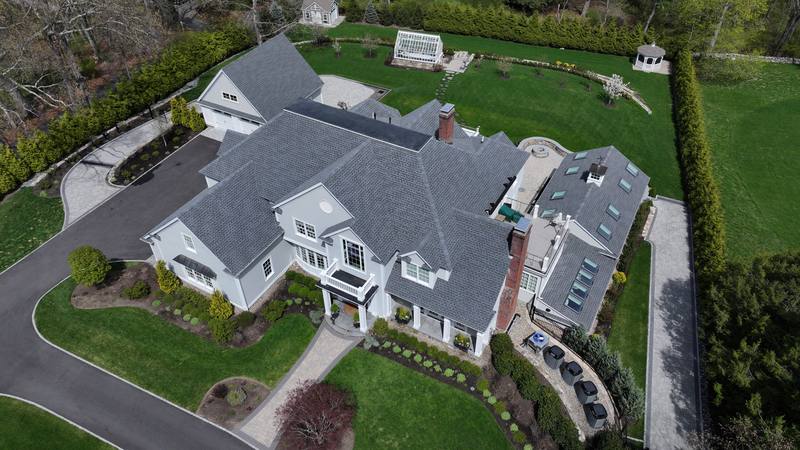 Large white home with a gray shingle roof on a landscaped lot, aerial view