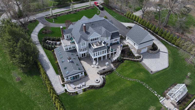 Gray shingle roof with skylights over a home with a stone patio, aerial view