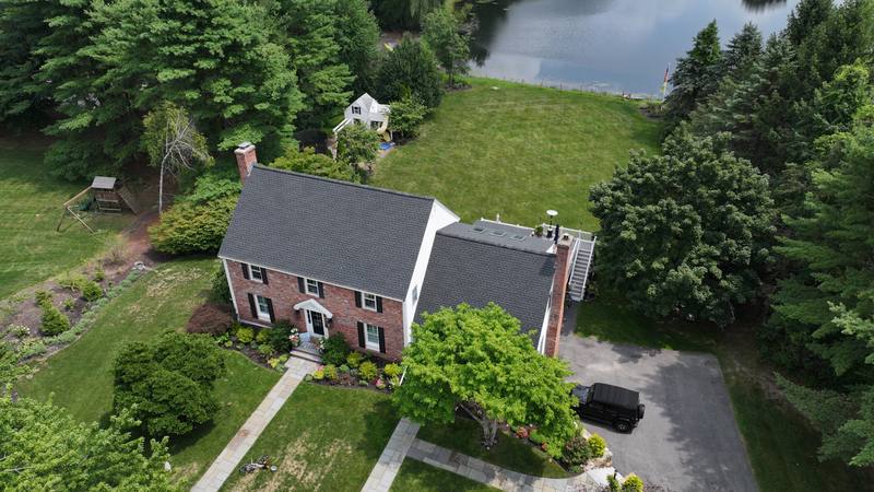 Brick-front colonial with a dark shingle roof near a pond